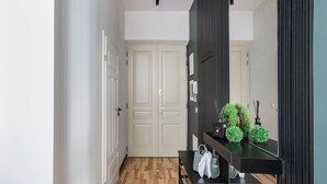 Un couloir doté d’un plancher en bois, une console noire ornée d’objets décoratifs et une porte blanche au fond.