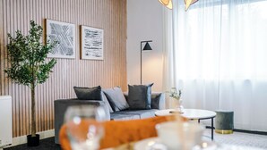 A modern living room with a sofa, a coffee table, and a dining table set for two. There are framed artworks on the wall and a potted plant. - Elm Apartments (Salford)