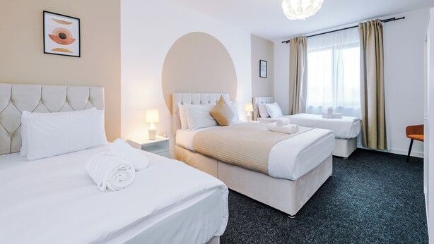 A hotel room with two beds, a large arched window, and a chandelier. - Elm Apartments (Salford)