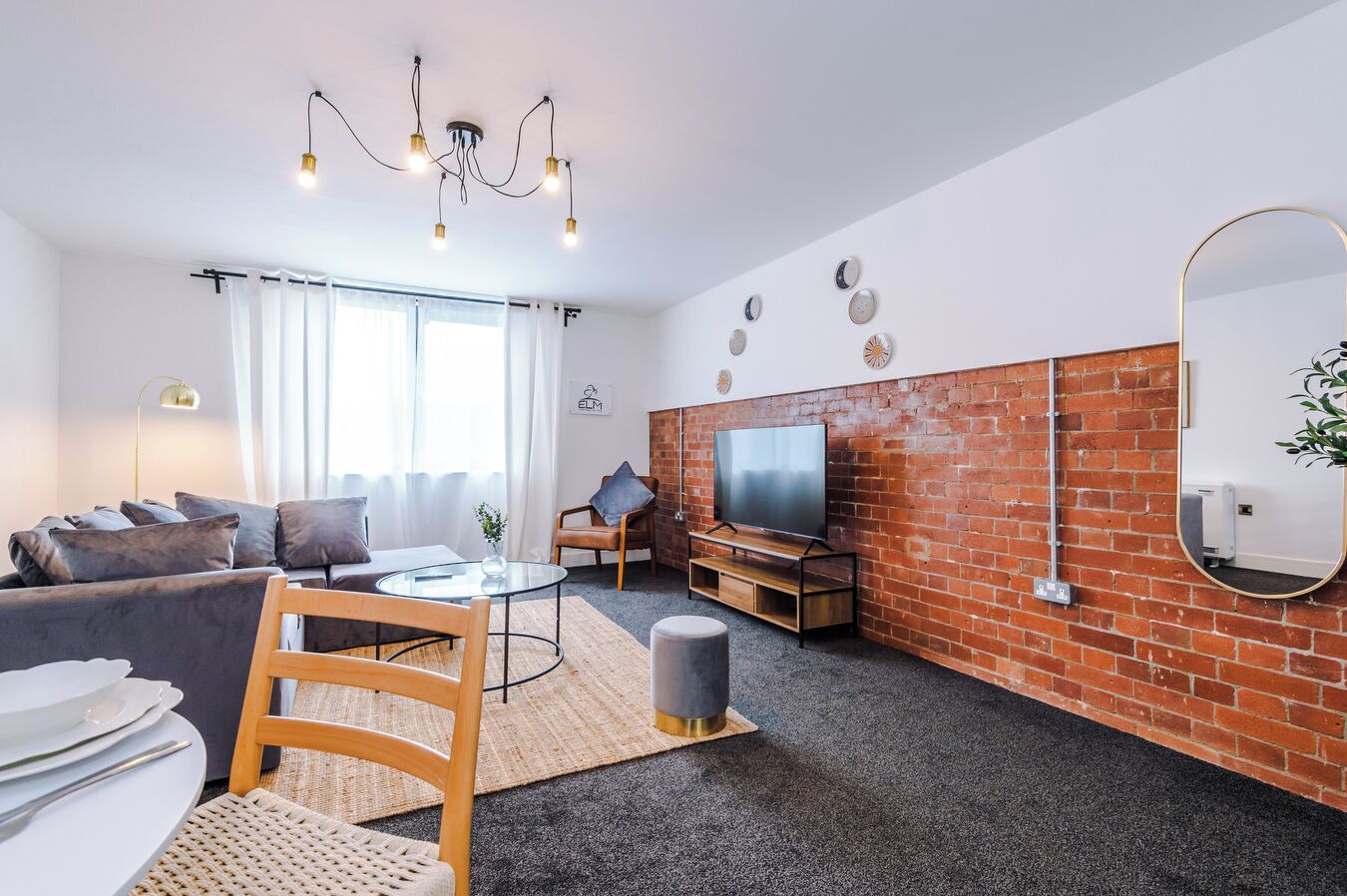 A modern living room with a sofa, a coffee table, a TV, and a brick accent wall.
