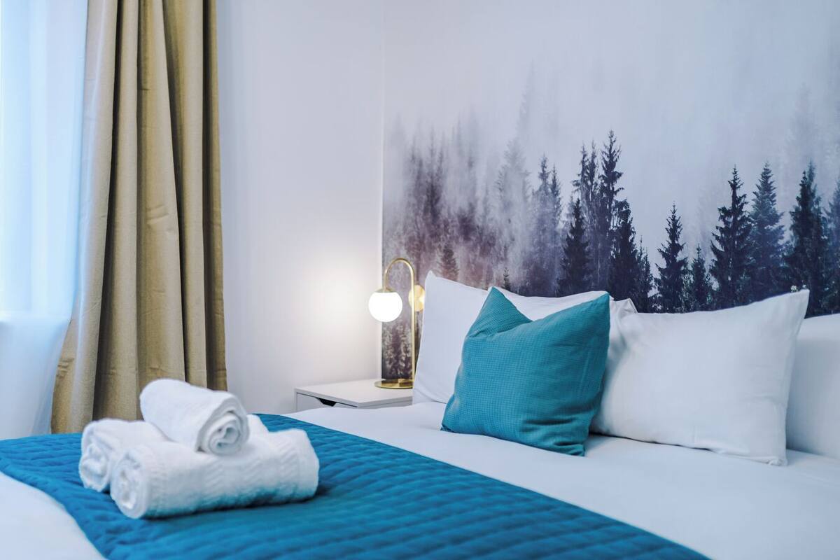 Une chambre d’hôtel avec un lit, une table de chevet, une lampe et une fresque murale sur le thème de la forêt.