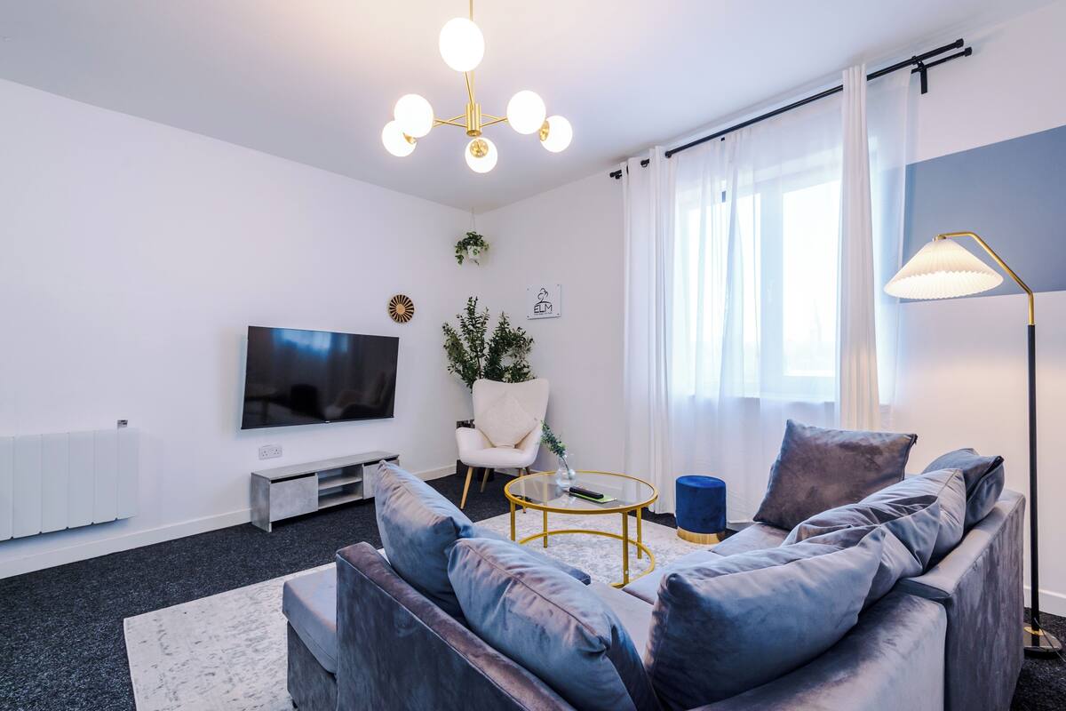 Un salon moderne avec un canapé gris, une table basse en verre, un téléviseur et un lampadaire.