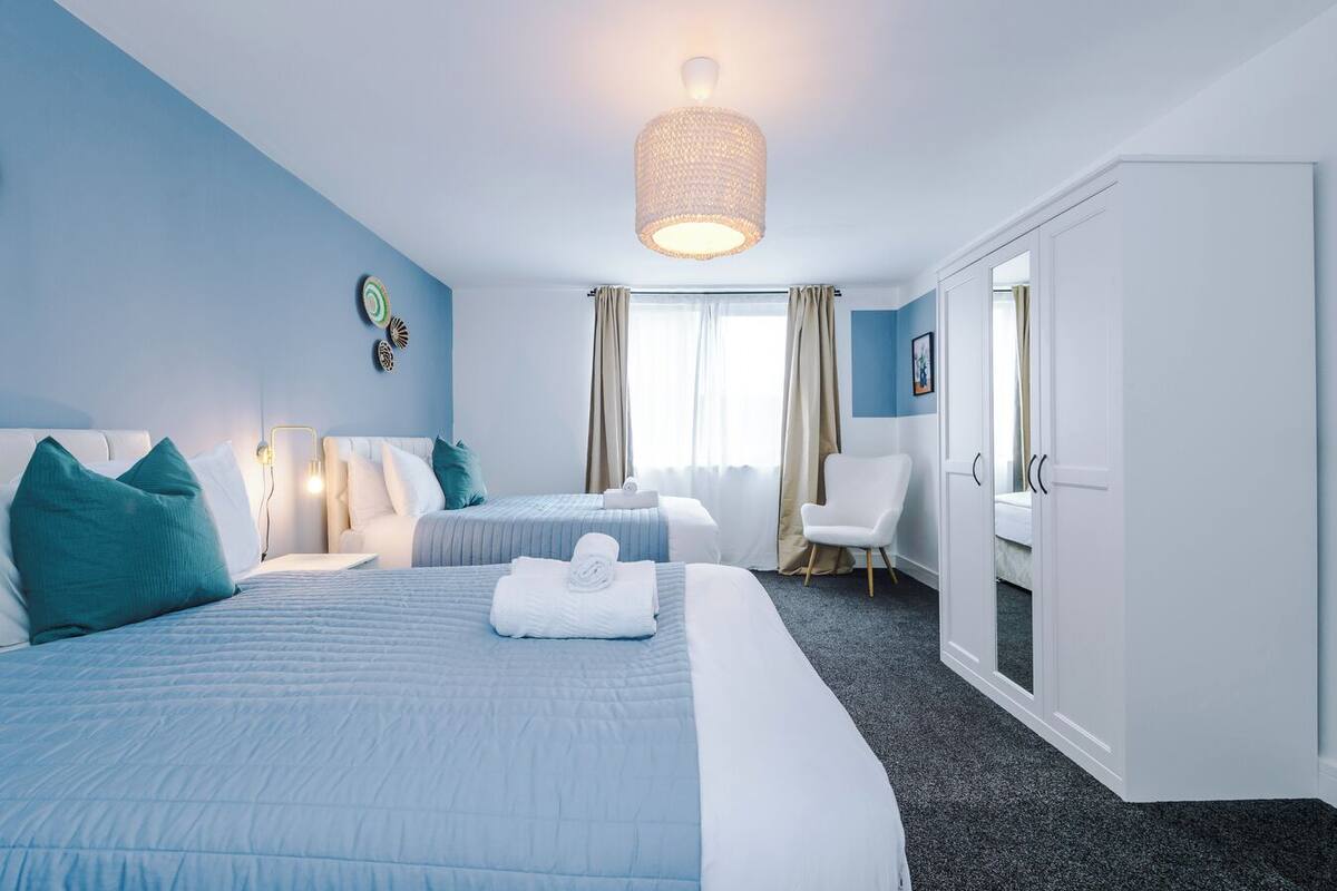 Une chambre d’hôtel avec deux lits, un coin salon, une armoire et une grande fenêtre avec des rideaux.