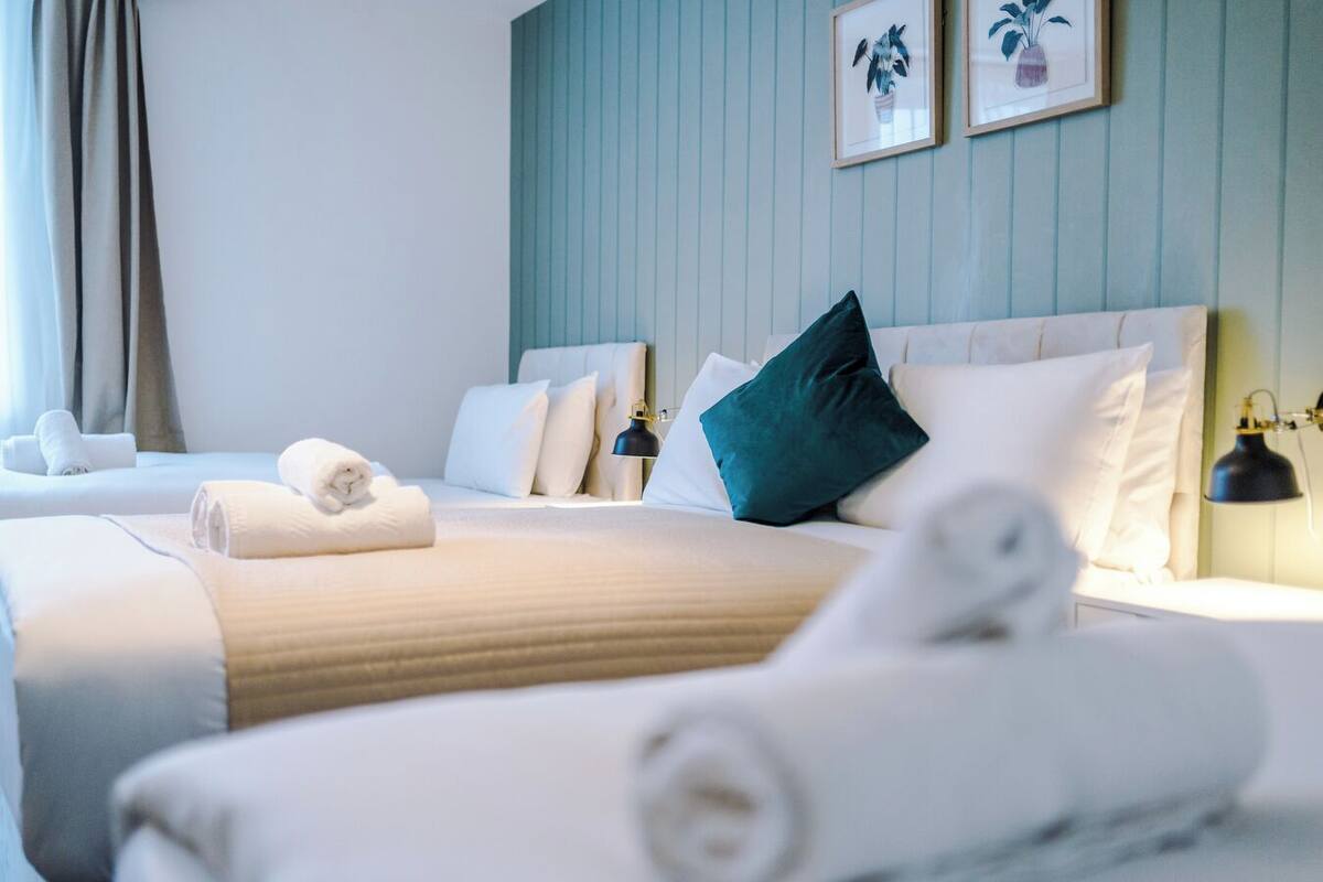Une chambre d’hôtel avec deux lits, du linge de lit blanc, un mur d’accent de couleur turquoise et deux tableaux représentant des plantes.