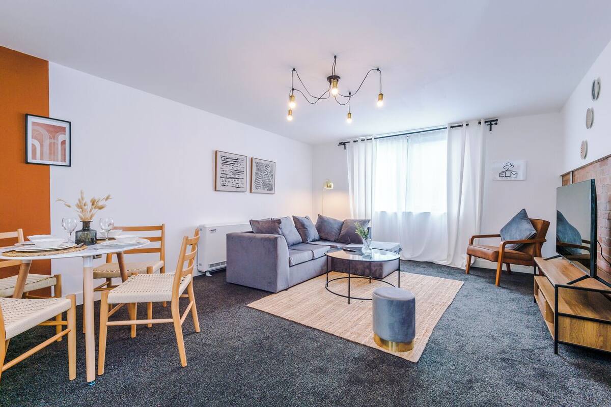 Un salon moderne avec un canapé gris, des chaises en bois, une table basse et un téléviseur.
