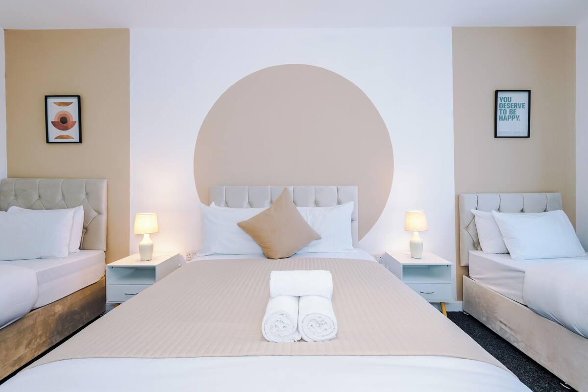 Une chambre d’hôtel avec deux lits, un grand élément de décoration circulaire au mur et deux affiches encadrées à message inspirant.
