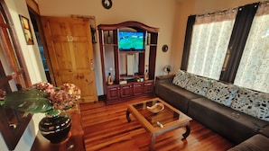Uma sala de estar com piso de madeira, um sofá, uma mesa de centro, uma televisão e uma porta.