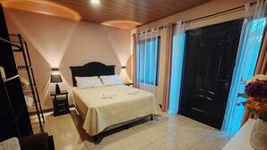 Quarto de hotel com cama, escrivaninha, cadeira, mesa de cabeceira, abajur, janela com cortinas e porta.
