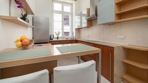 Cocina moderna con encimera de madera, sillas blancas, un cuenco de fruta y una ventana con vistas a edificios.