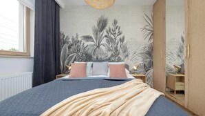 Quarto com cama, janela, parede decorada com um mural de plantas e um guarda-roupa.
