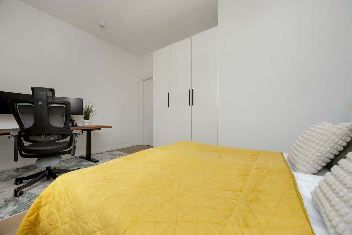 Une chambre avec un couvre-lit jaune, un bureau avec une chaise et une armoire.