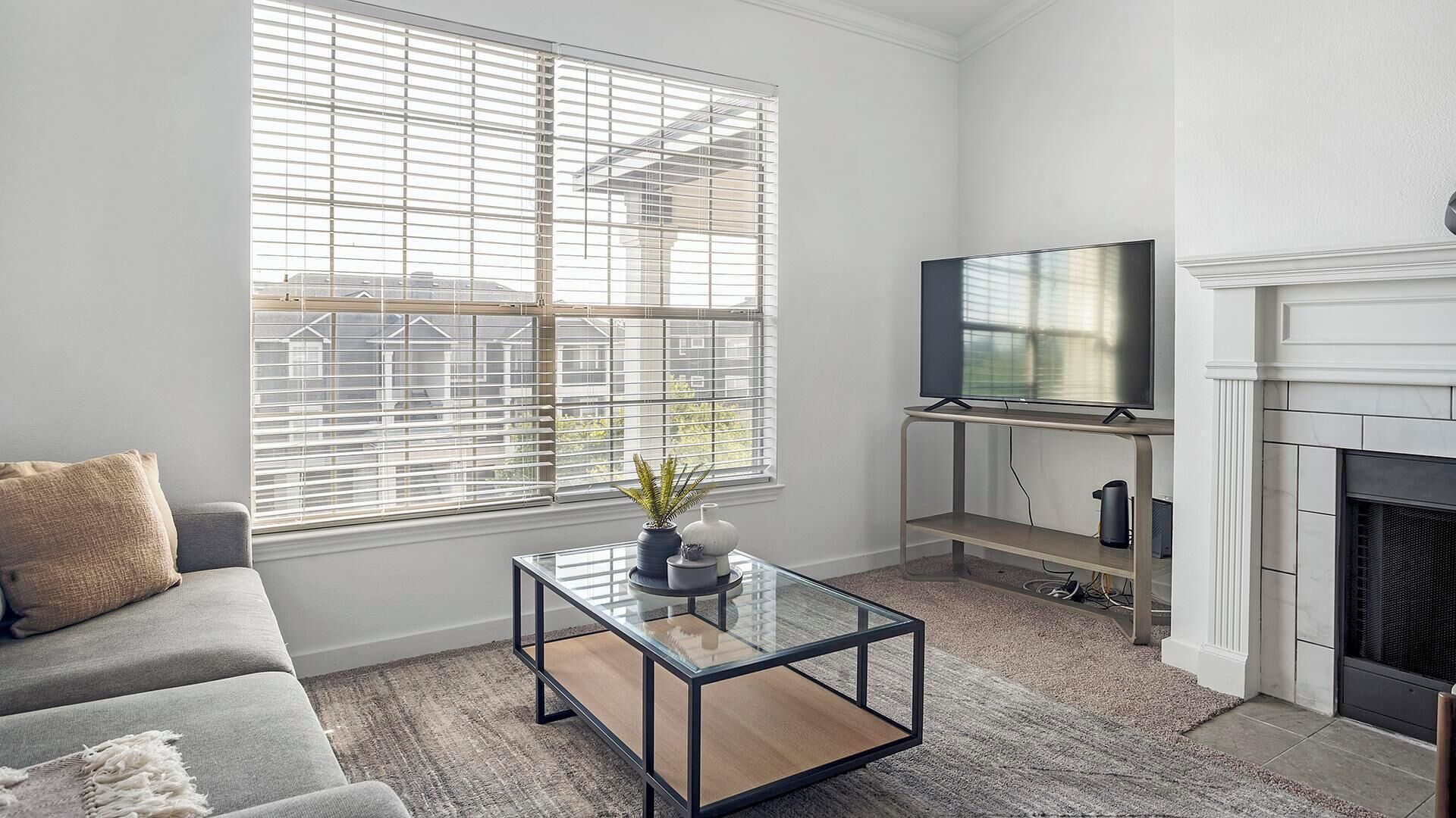 A modern living room with a sofa, a glass coffee table, a flat-screen TV, and a fireplace.