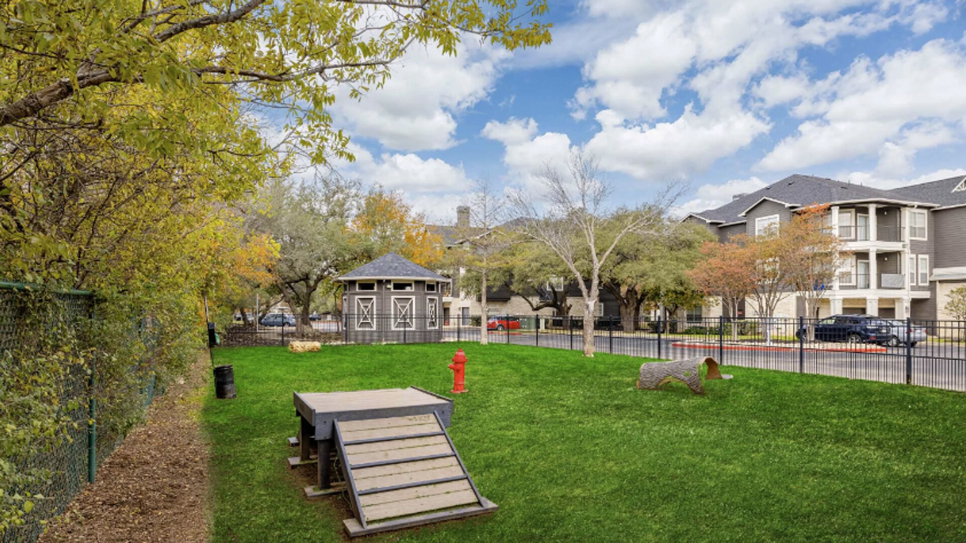 A grassy outdoor area with a wooden bench, a small shed, and a red fire hydrant.