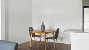 A small, modern room with a round wooden table and two black chairs. There is a vase on the table, and the room has a white wall and carpet. - Landing | Amazing 2BD, Pool, Clubhouse (Austin)