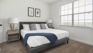 A bedroom with a bed, two bedside tables, a window with blinds, and two framed pictures on the wall. - Landing | Amazing 2BD, Pool, Clubhouse (Austin)