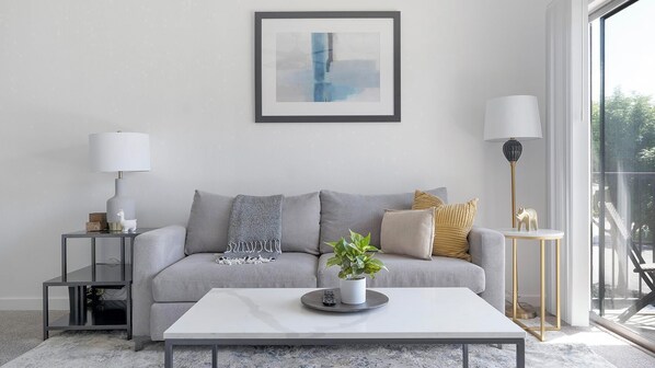 A modern living room with a grey sofa, a white coffee table, and a framed abstract painting on the wall. - Landing | Incredible 1BD, Gym, Pool (Austin)