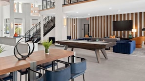A modern hotel lobby with a pool table, seating area, and a staircase.