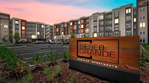 A sign for Deséo Grande Premier Apartments with a modern multi-story building in the background.