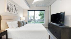 A modern bedroom with a large bed, a TV, and a view of a residential area.