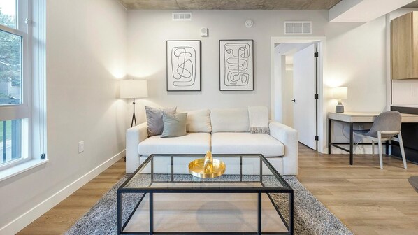 A modern living room with a white sofa, a glass coffee table, and two abstract art pieces on the wall.