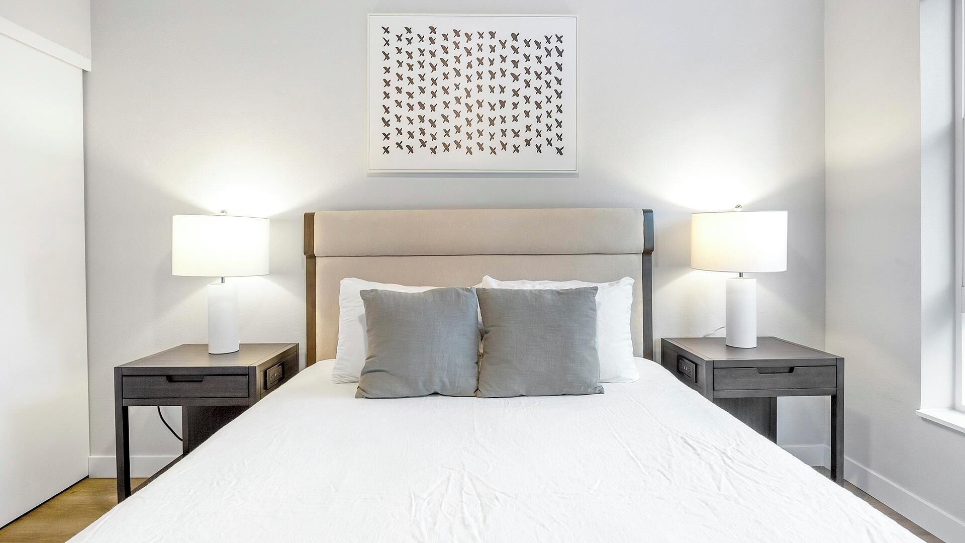 A neatly made bed with two pillows, two bedside tables with lamps, and a wall-mounted artwork above the bed.