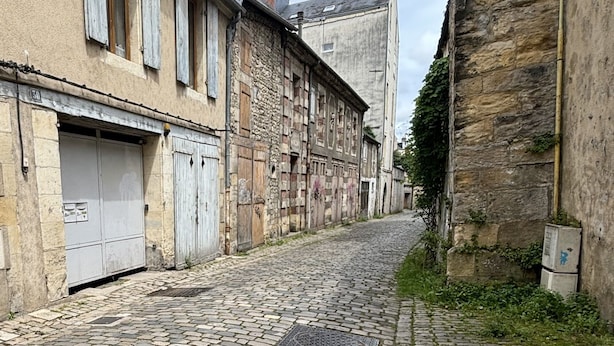 A cobblestone street flanked by historic buildings with stone facades and wooden shutters. - Charming apartment with character (Nevers)