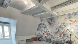 A conference room with a round table, grey chairs, a mural of flamingos, and a modern ceiling design. - Charming apartment with character (Nevers)