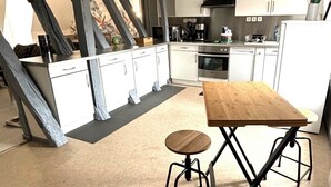 A modern kitchen with white cabinets, a wooden table, and a small stool. - Charming apartment with character (Nevers)