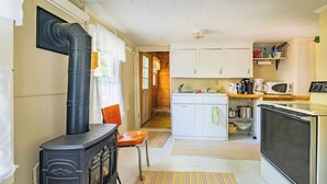 A compact kitchen with a wood-burning stove, white cabinets, and a microwave. - Sweet Thing Summary: (Portland)