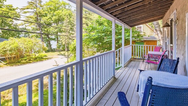 A covered porch with a wooden ceiling, white railings, and a view of a road and greenery. - Sweet Thing Summary: (Portland)