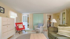 A cozy living room with a red armchair, a green sofa, a white dresser, and a wicker chair. - Sweet Thing Summary: (Portland)