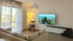 En stue med sofa, lampe, stol og et tv på væggen, der viser et naturskønt udsigt.