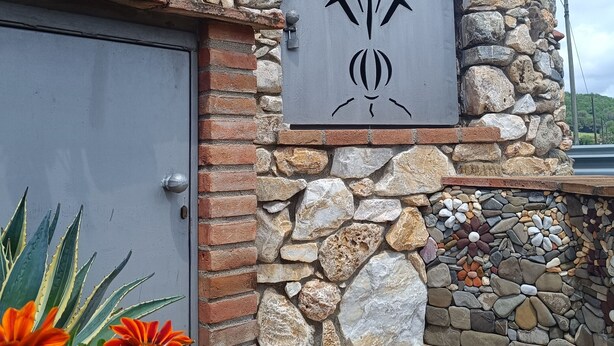 Facciata in pietra con porta in metallo e un emblema decorativo.