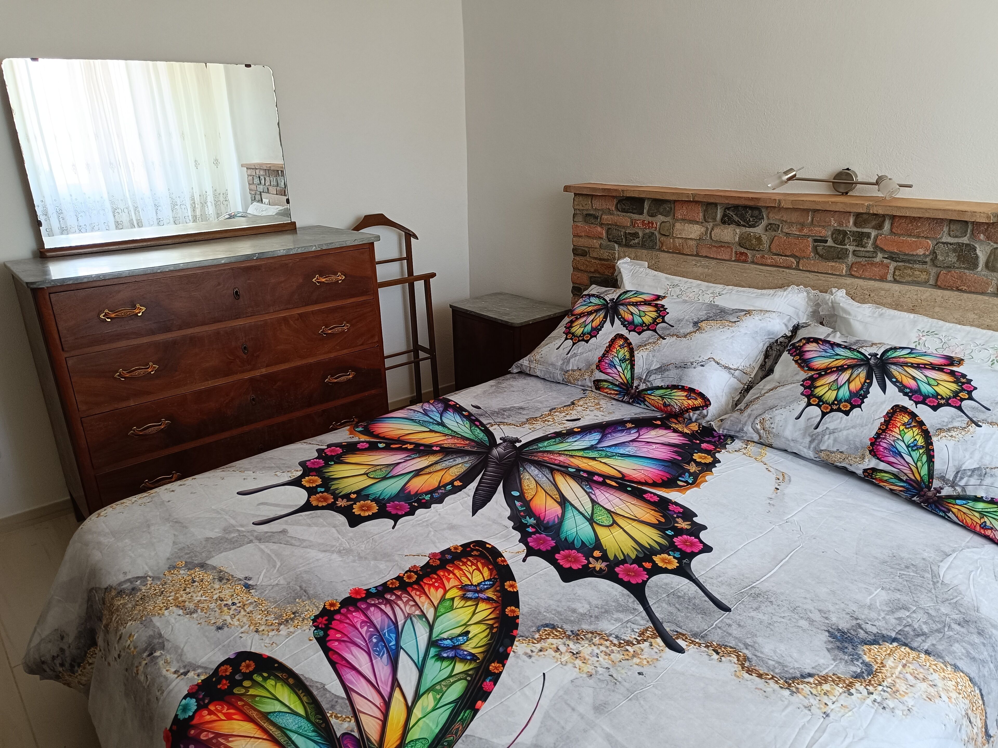 A bedroom with a bed featuring butterfly-themed bedding, a wooden dresser, and a brick accent wall.