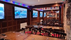Un ristorante con diversi tavoli e sedie, un'area bar e due grandi schermi che mostrano una pubblicità di automobili.
