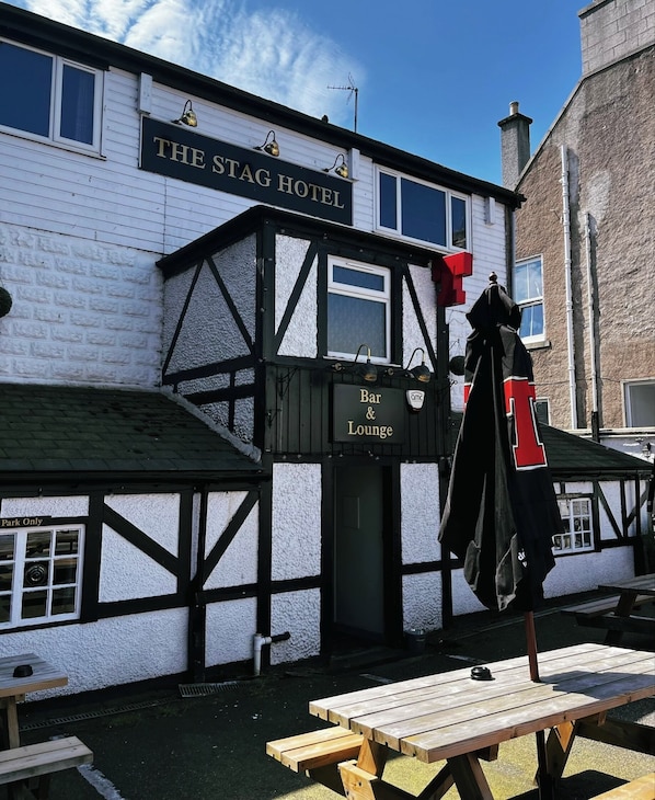 The Stag Hotel with a Bar & Lounge sign, wooden exterior, and picnic tables outside.