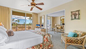 A hotel room with a bed, a desk, a chair, and a balcony with a view of palm trees.