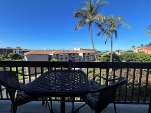 A balcony with a table and chairs, overlooking a residential area with palm trees and buildings.