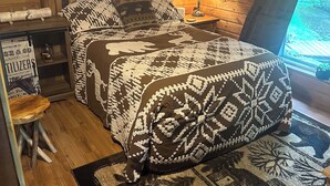 Una camera da letto accogliente in stile baita, con arredamento in legno, un letto con biancheria a motivi, un comodino con una lampada e vista sull'esterno.