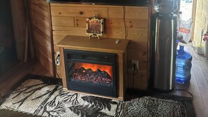 Un accogliente interno di una baita con camino, una TV a schermo piatto montata su una parete in legno e un distributore d'acqua.