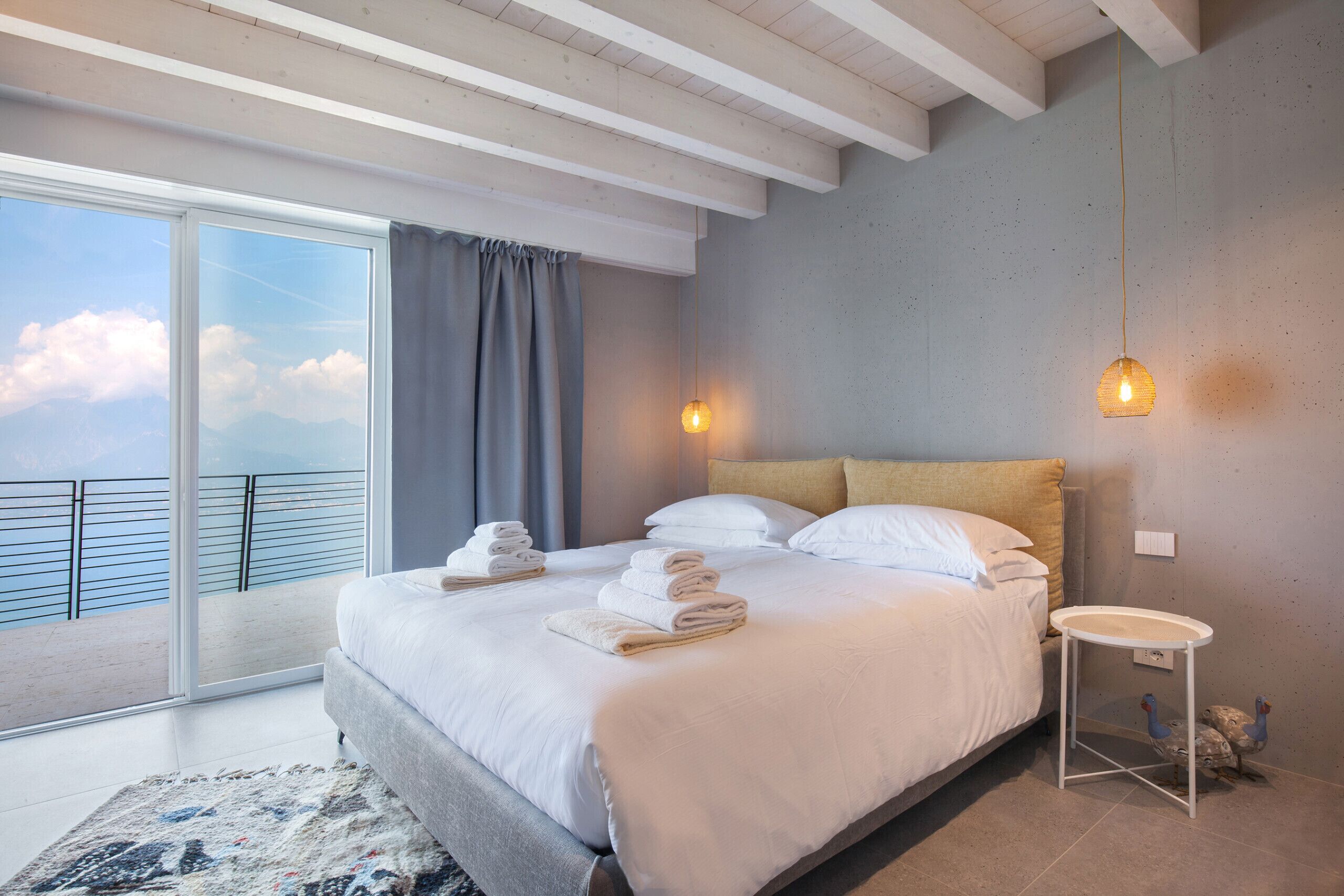 Een moderne hotelkamer met een groot bed, een klein nachtkastje en uitzicht op de lucht vanaf een balkon.