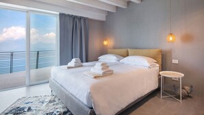 A modern hotel room with a large bed, a small bedside table, and a view of the sky through a balcony.