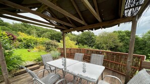 An outdoor patio with a wooden deck, a table with chairs, and a pergola overhead.