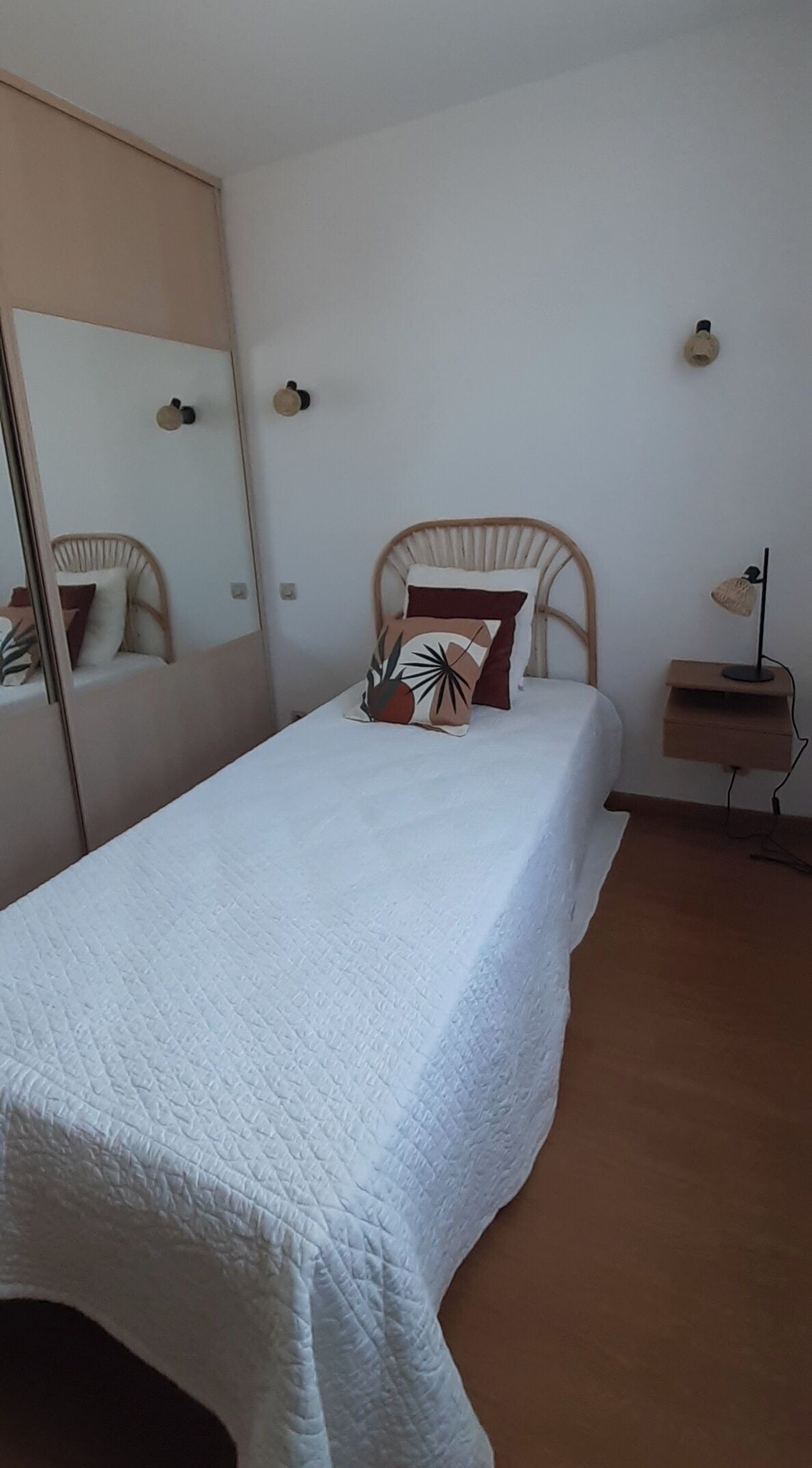 Et soveværelse med seng, natbord, lampe, spejl og garderobeskab.