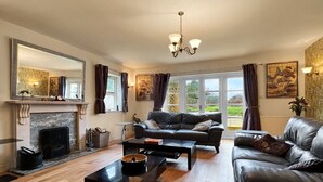 A living room with a fireplace, leather sofas, a coffee table, and large windows with curtains.