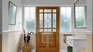 A wooden door with a grid pattern, a wicker basket with umbrellas, and a white cabinet with a green vase.