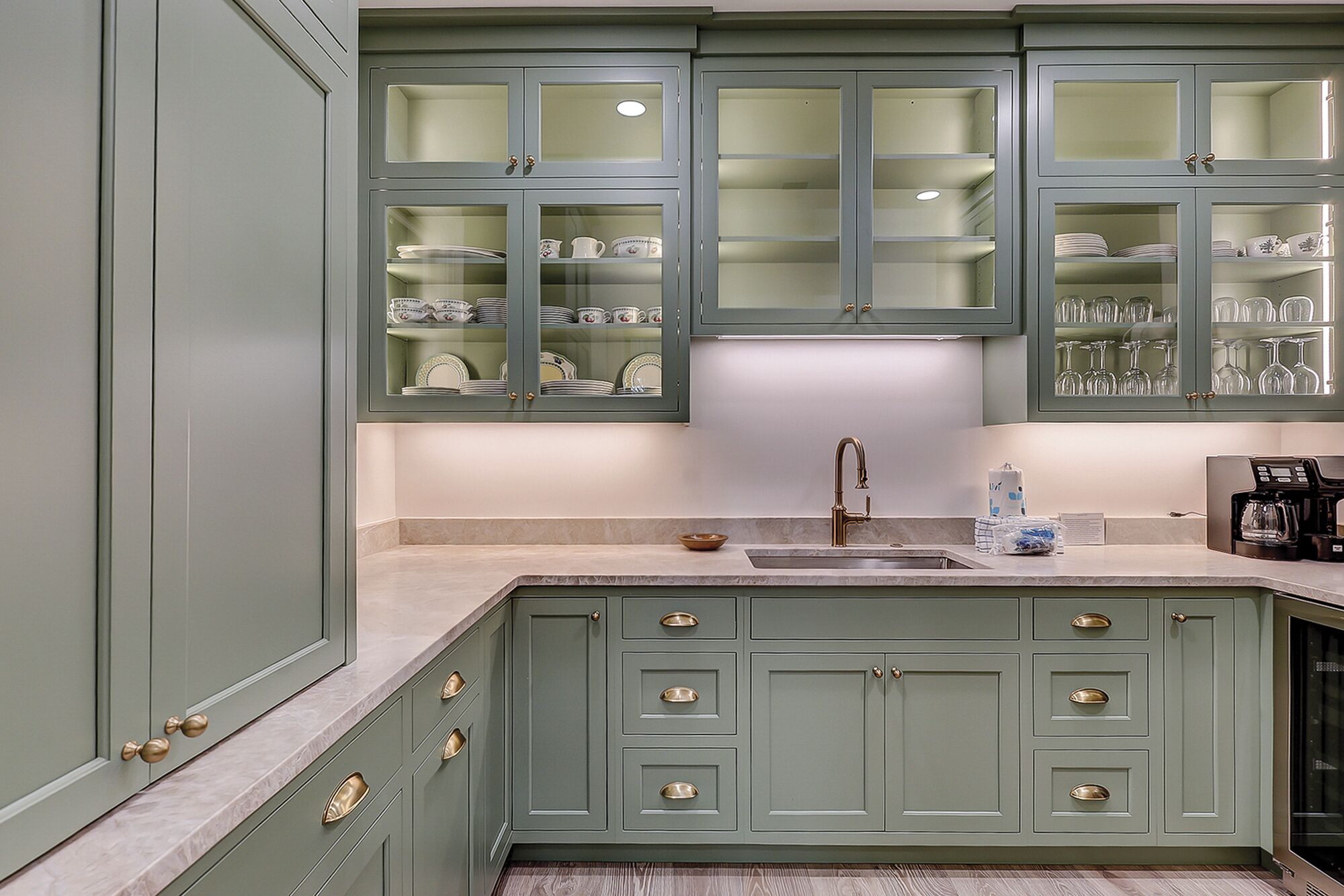 A kitchen with green cabinets, a sink, and a coffee maker.