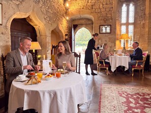 A stone-walled dining area with round tables, a waiter serving, and a view of the outdoors. - Abbots Grange Manor House (Broadway)