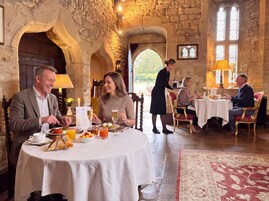 A stone-walled dining area with round tables, a waiter serving, and a view of the outdoors.