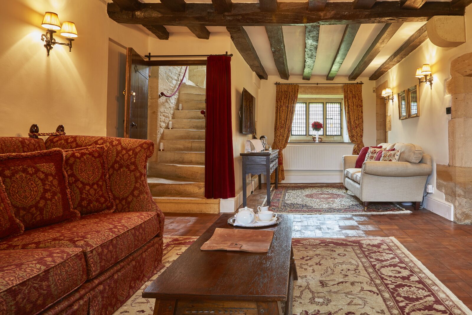 A cozy living room with a patterned sofa, a wooden coffee table, and a staircase leading to a bedroom.
